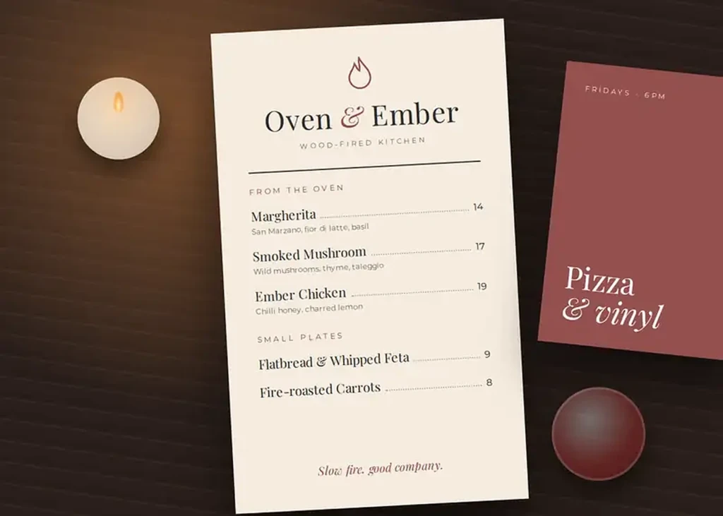 Oven & Ember menu and event poster on a dark wooden table by candlelight